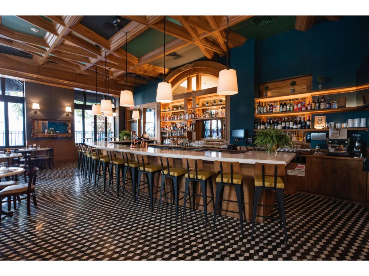 A chic interior scene spotlights an elegant bar counter lined with bottled spirits, beneath a decorative ceiling. The space is softly lit, creating an intimate, upscale atmosphere perfect for socializing and enjoying handcrafted cocktails or small plates.