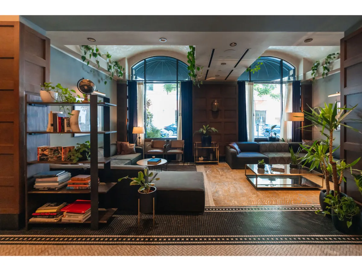 A spacious, light-filled lounge with large windows, comfortable seating, bookshelves filled with books and plants, and a coffee table with decorative elements. The mood is relaxed and inviting, ideal for unwinding after a workout or planning an urban exploration.