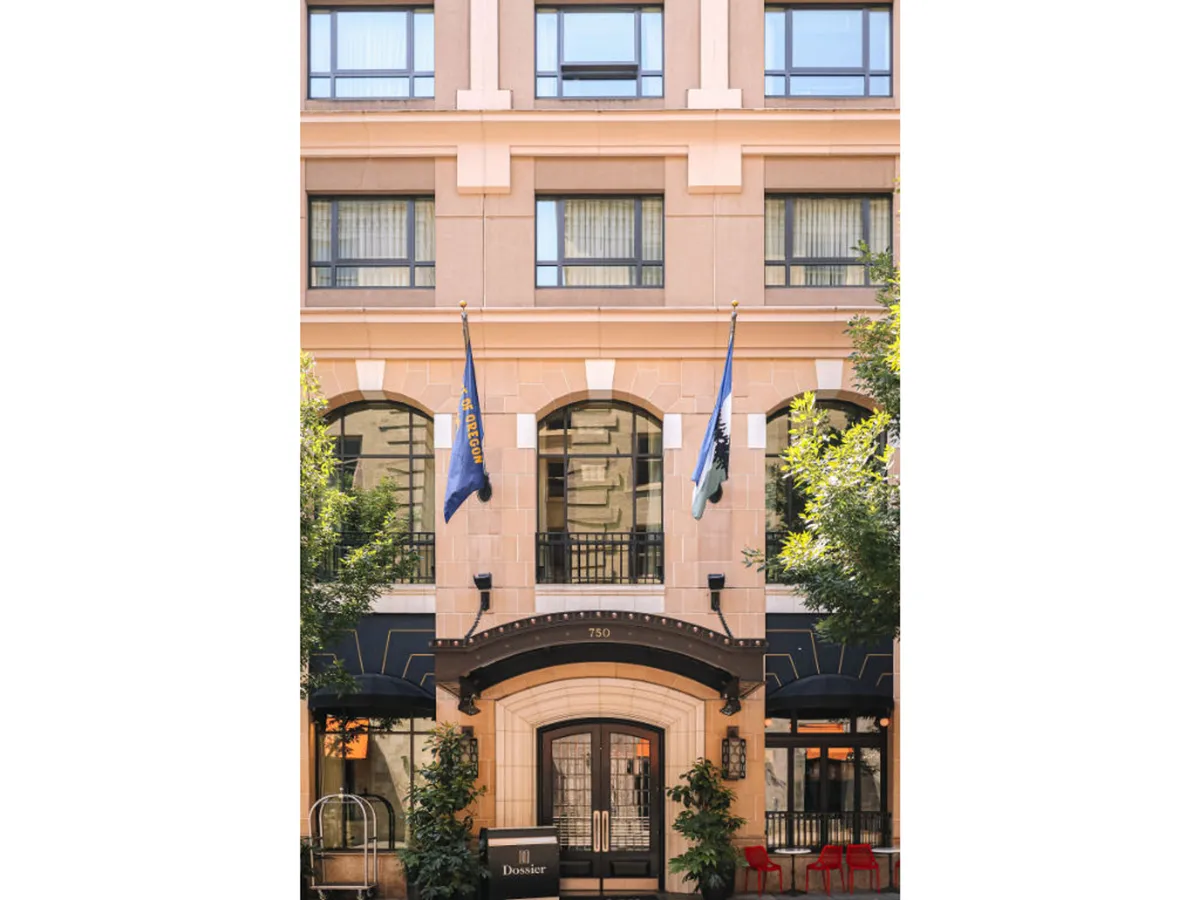 The photo provides a welcoming, broad view of the hotel’s main entrance, with decorative flags and distinctive architecture. Guests are pictured socializing just in front of the building, hinting at the hotel’s central role in the neighborhood.