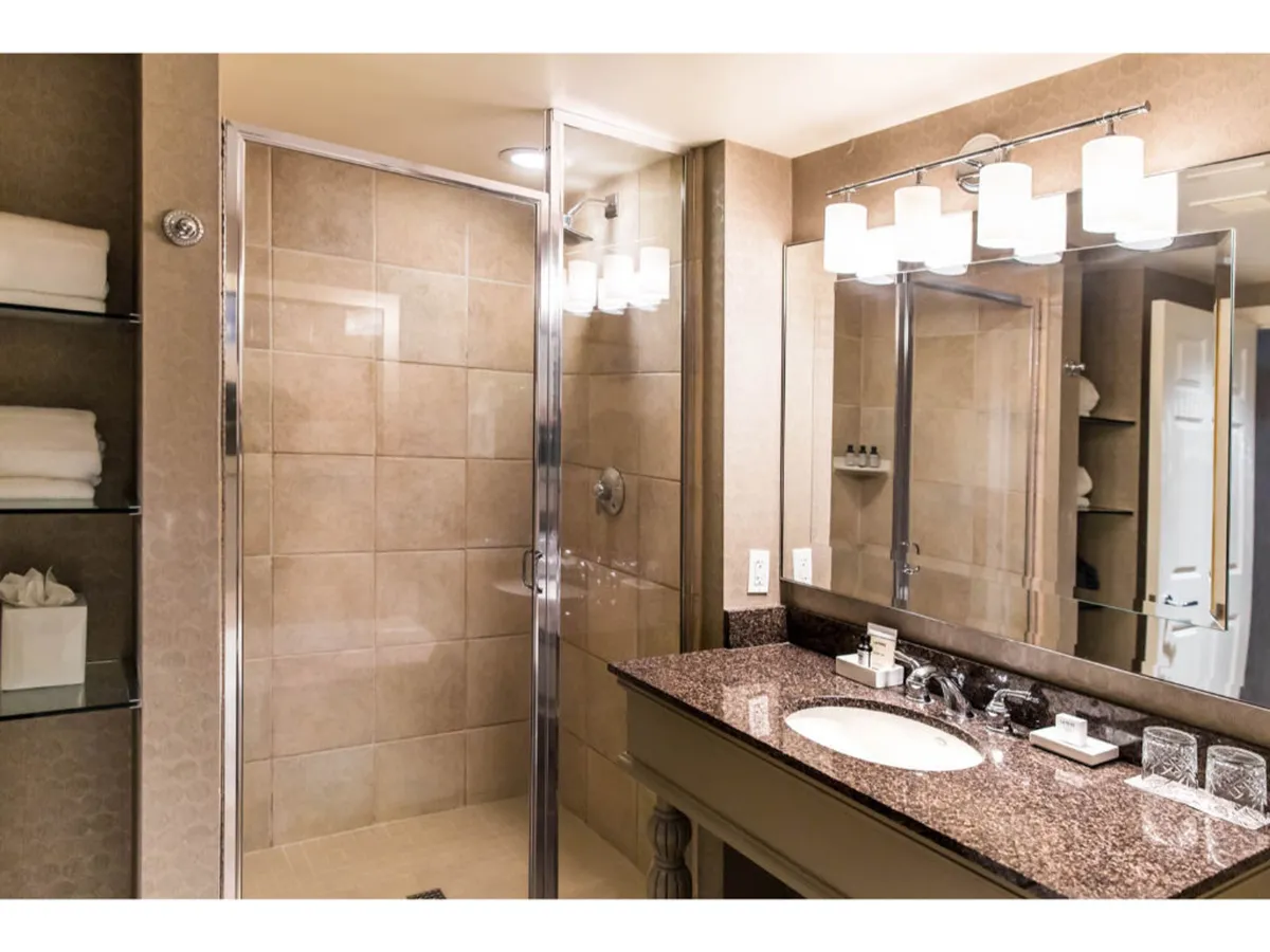 A bright, elegant bathroom with a granite countertop, modern fixtures, and a glass-enclosed standalone shower. The well-lit mirror and clean lines create an inviting space for self-care routines.