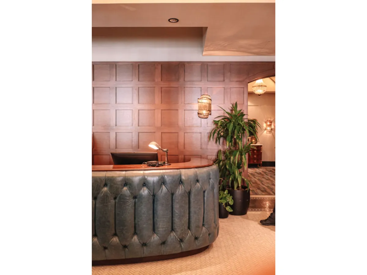 This image features a stylish, curved reception desk set against warm wood paneling and illuminated by contemporary hanging light fixtures. A potted plant adds a welcoming touch, and the overall atmosphere is inviting and sophisticated, suggesting attentive service and a polished arrival experience.