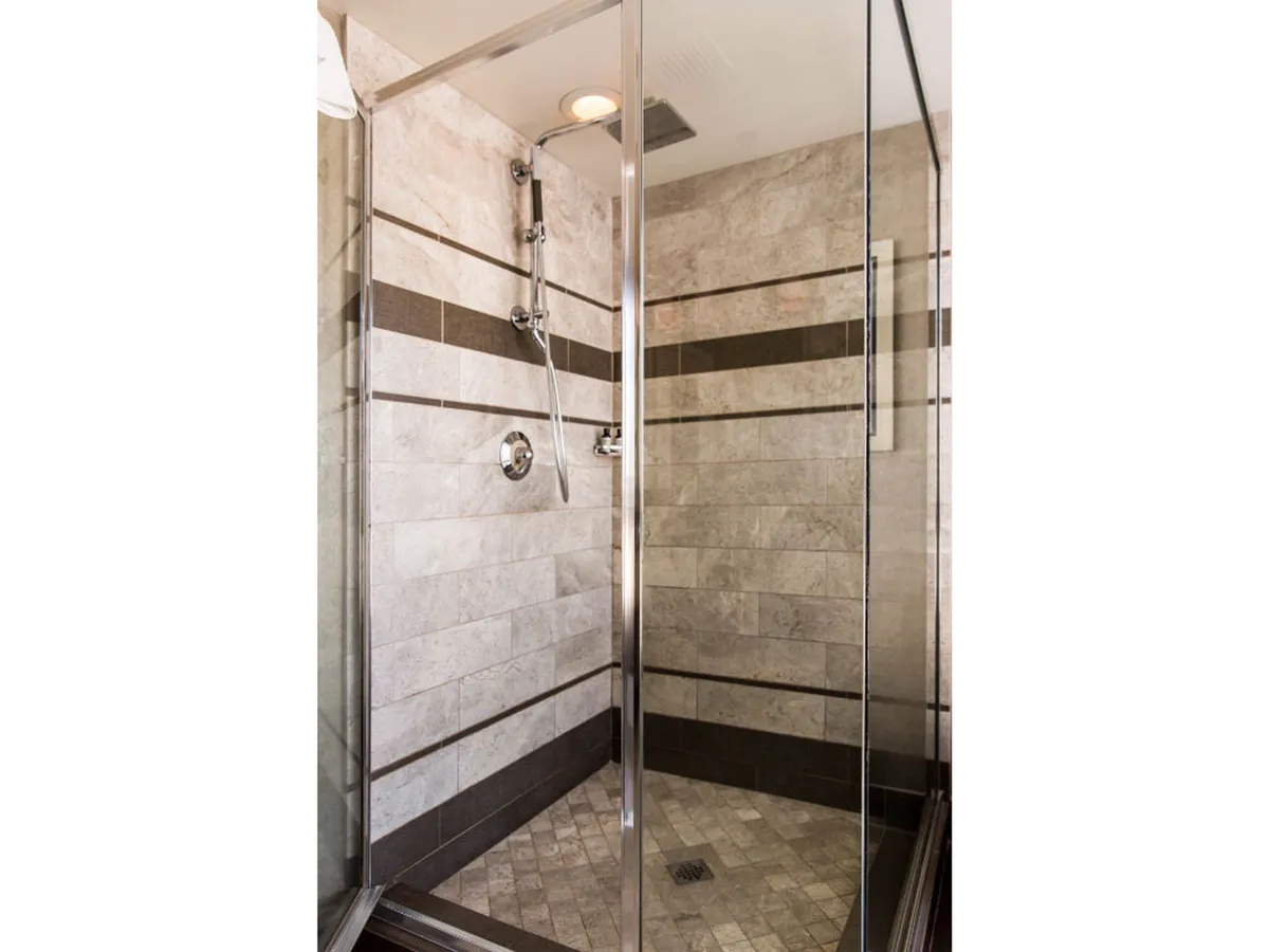 A serene, spa-like bathroom showcases a glass-enclosed shower with modern fixtures and textured tiles. The calming atmosphere invites guests to unwind and enjoy premium bath amenities.
