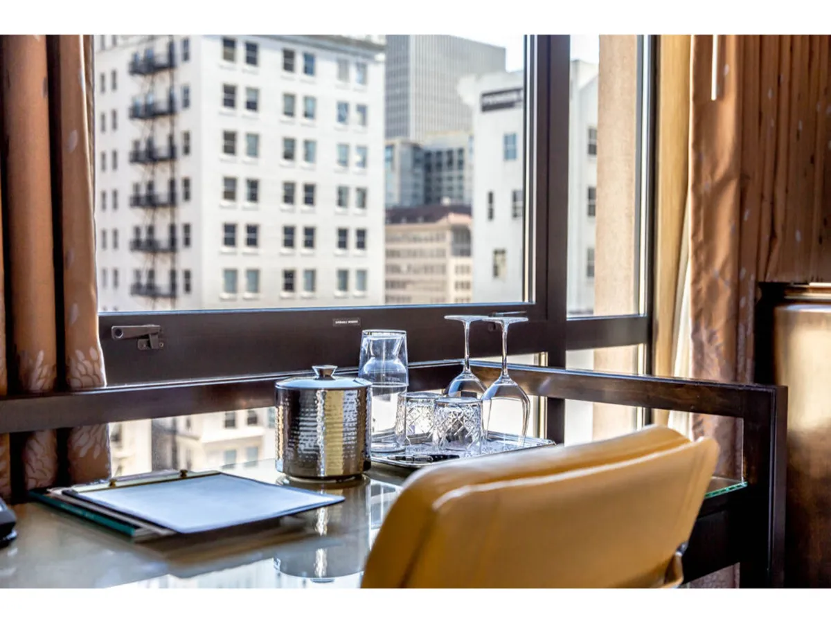 The image showcases a beautifully arranged desktop in a premium hotel room. On the desk are elegant glass water bottles, an ice bucket, and a notepad with a pen, all placed beside large windows that offer sweeping city views. The setup invites guests to enjoy a quiet moment of productivity or relaxation while overlooking Portland's vibrant skyline.